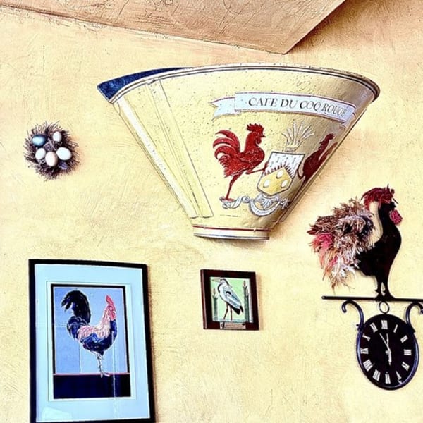 Rooster-themed decor on a yellow wall, including a large funnel, framed art, and a clock.