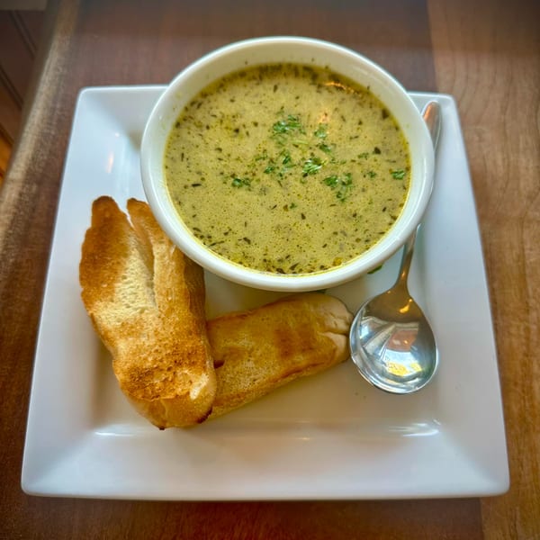 Creamy green soup with herbs, served in a white bowl with toasted baguette slices and a spoon.