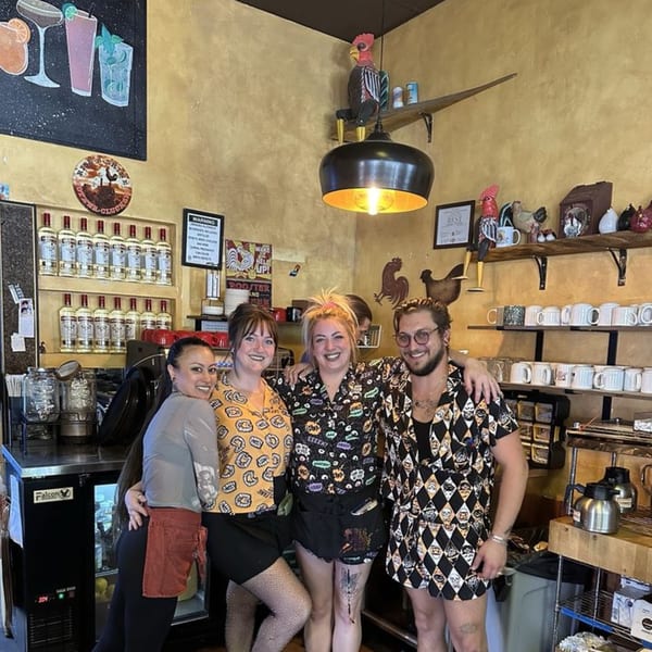 Four smiling cafe employees pose together behind the counter at Old Town Red Rooster Cafe.