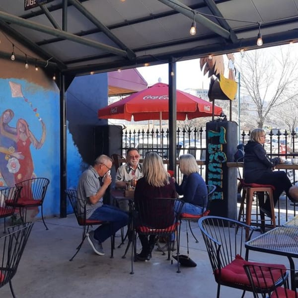 Patrons enjoying the outdoor patio seating at Old Town Red Rooster Cafe, with a colorful mural and red umbrellas.