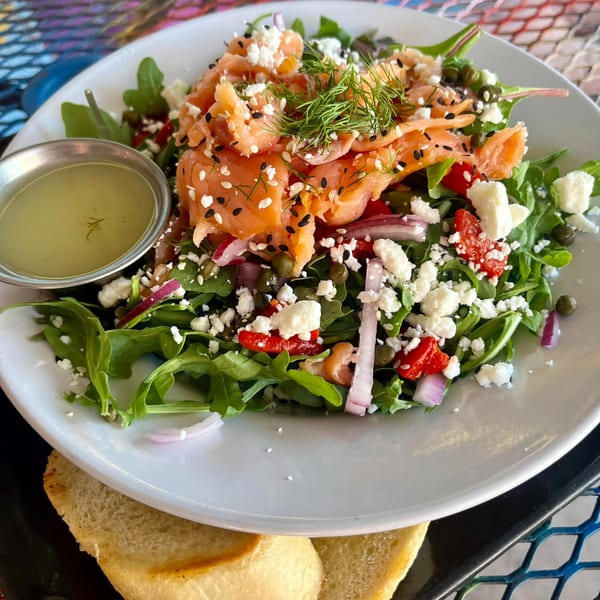 Smoked salmon salad with arugula, feta, capers, red onion, and dill, served with dressing and bread.