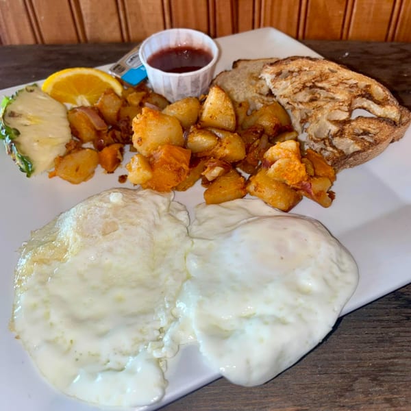 A breakfast plate with two fried eggs, home fries, toast, and a side of fruit.