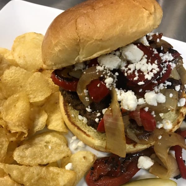 A burger with grilled onions, red peppers, and feta cheese, served with potato chips.
