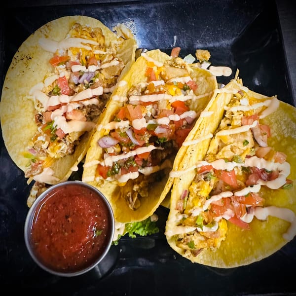 Three breakfast tacos with scrambled eggs, pico de gallo, and sauce, served with a side of salsa.