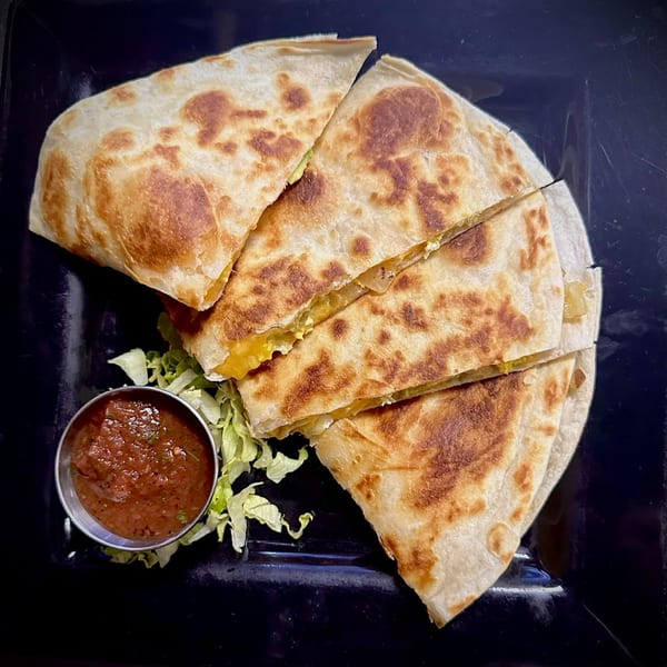 Golden-brown quesadilla wedges with melted cheese, served with salsa and shredded lettuce on a black plate.