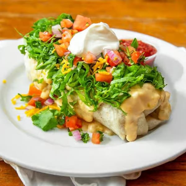 A large burrito covered in cheese sauce, lettuce, pico de gallo, and sour cream, with salsa on the side.